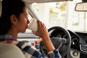 Mujer joven tomando cafe mientras maneja