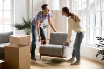 Hombre y mujer jovenes moviendo sillon en su apartamento