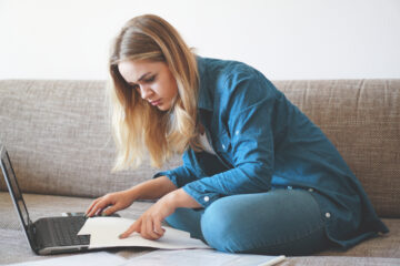 Mujer joven enfocada revisando computadora portatil buscando seguro médico