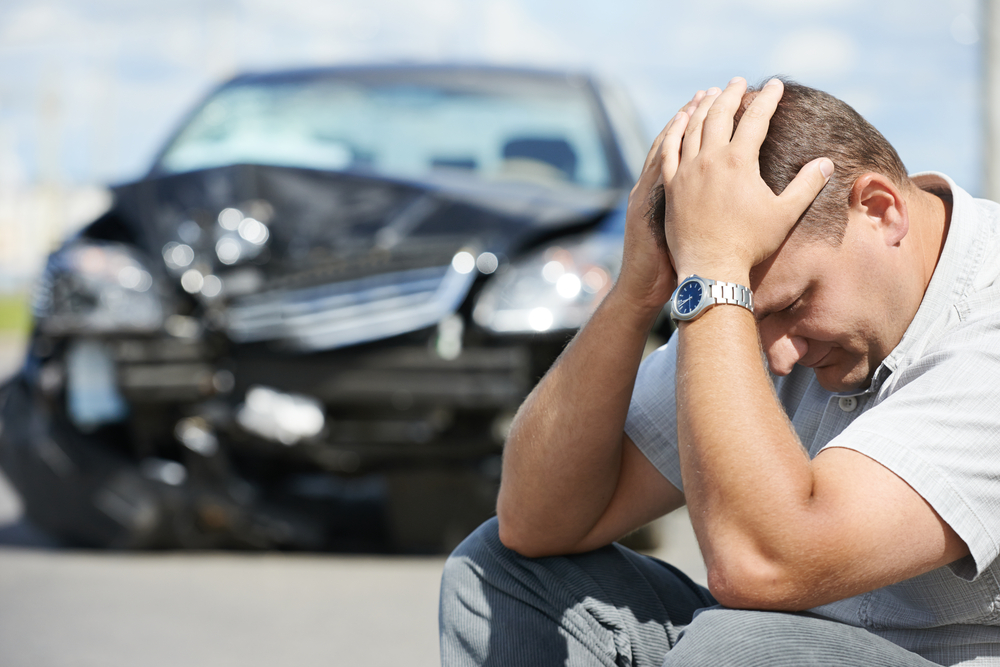 Hombre sentado en la carretera después de sufrir daños en su coche por un choque