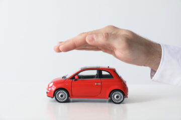 Imagen simbólica del seguro de auto en la que una mano se encuentra cubriendo un automóvil de juguete