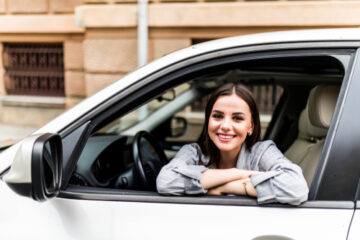 Mujer hispana sonriendo en su auto por tener seguro de automóvil