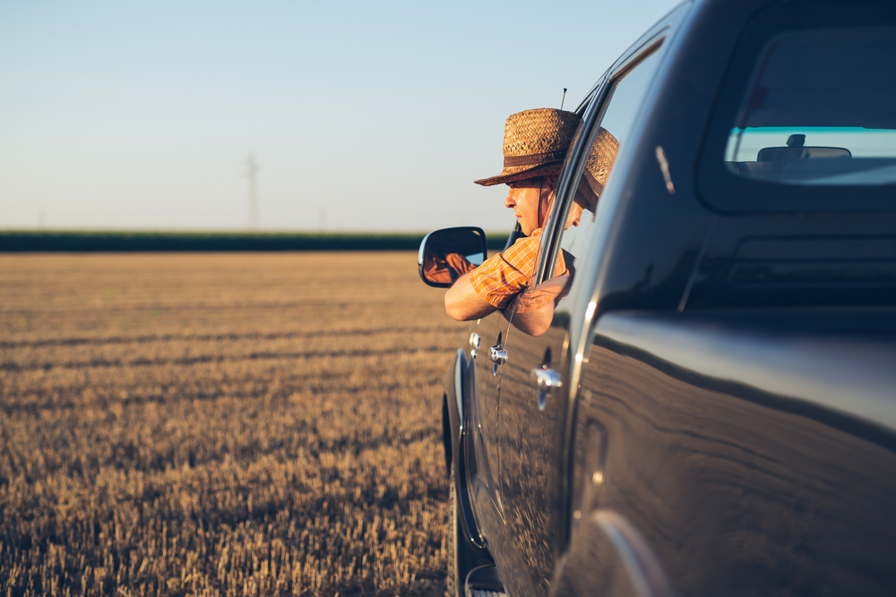 sideview of man with hat drivingpick up truck in a field