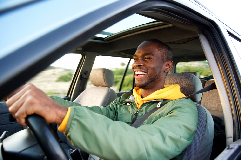 Side portrait of happy african american man driving with car insurance savings