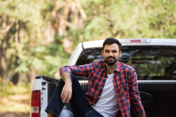 bearded man sitting on pickup truck in nature