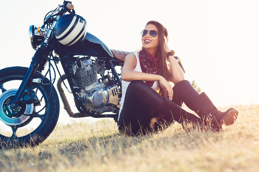 smiling woman sitting in front of her motorcycle in a field