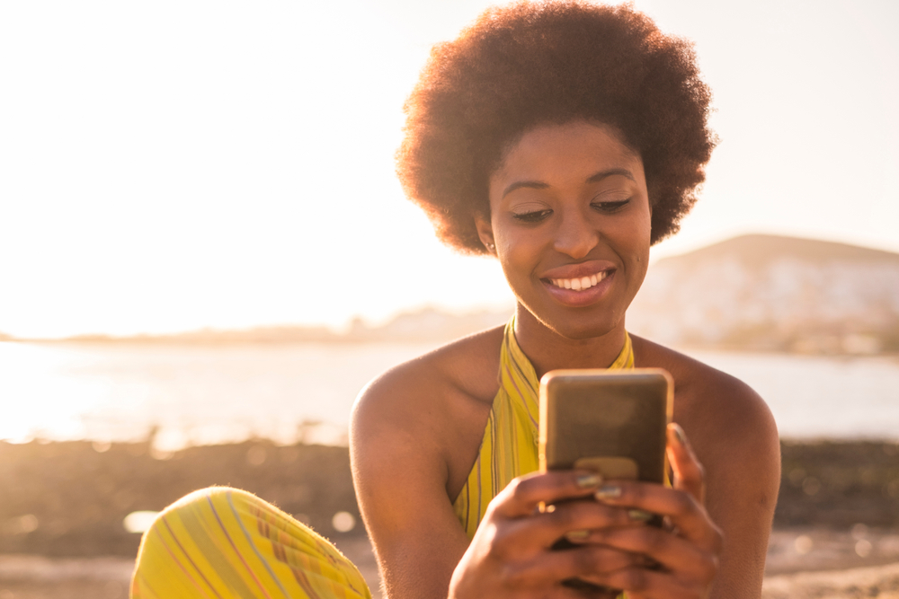 african american smiling woman looking in phone for car insurance