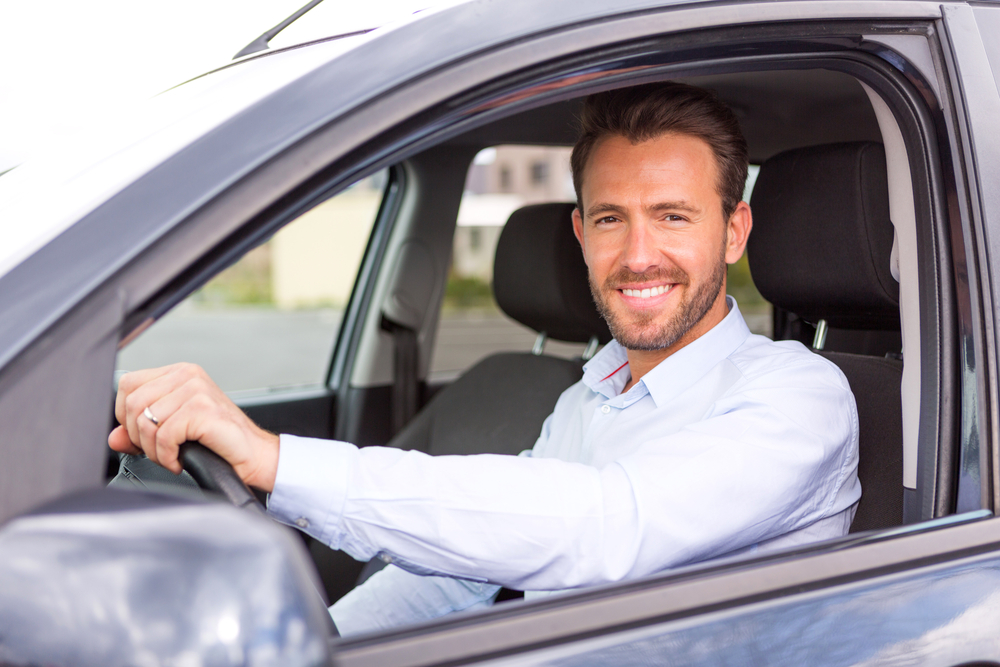 caucasian man smiling with hand on steering wheel of car