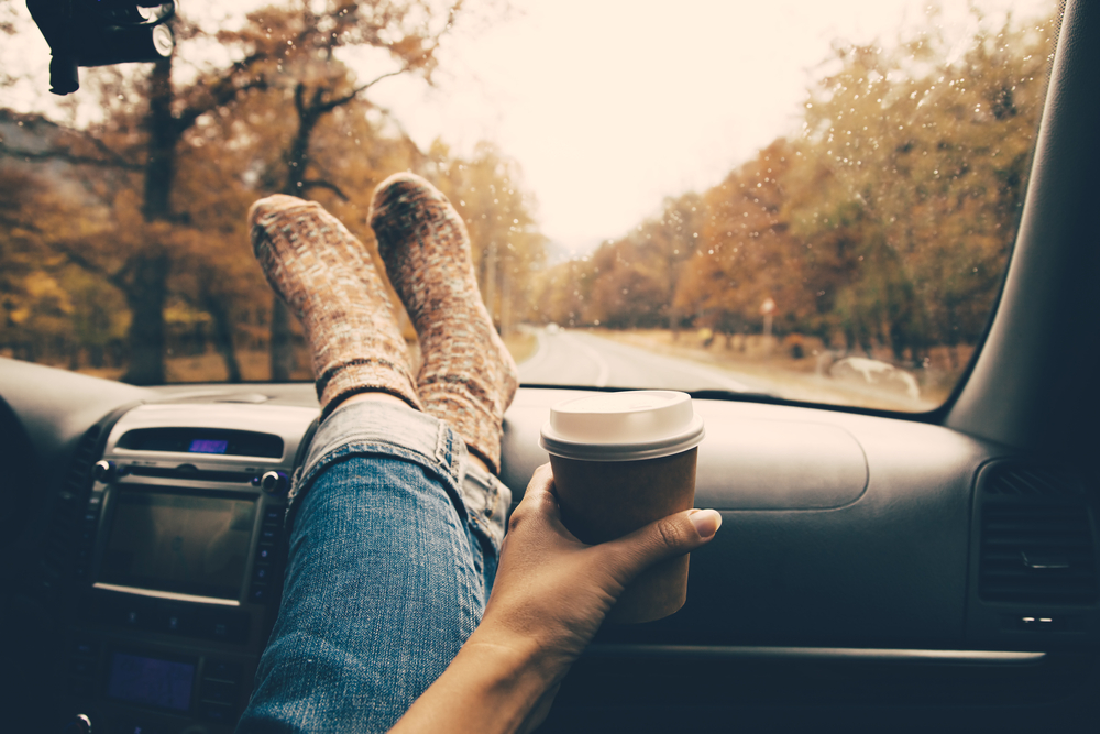 woman with legs on dashboard during fall road trip with coffee and socks on