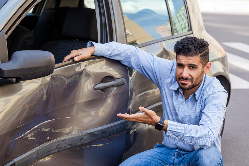 Young Hispanic man points to damage caused in a car accident
